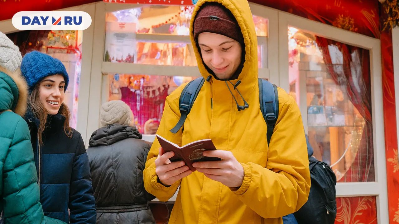 Молодой человек в жёлтой куртке читает буклет на рождественской ярмарке