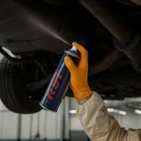 Механик наносит антикоррозийный спрей на автомобиля