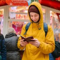 Молодой человек в жёлтой куртке читает буклет на рождественской ярмарке